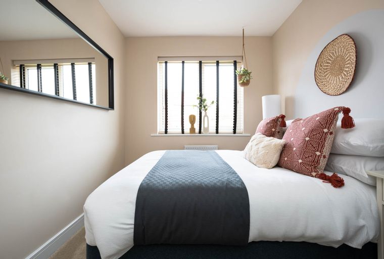 A bedroom with a bed, pillows, a window, and a mirror.