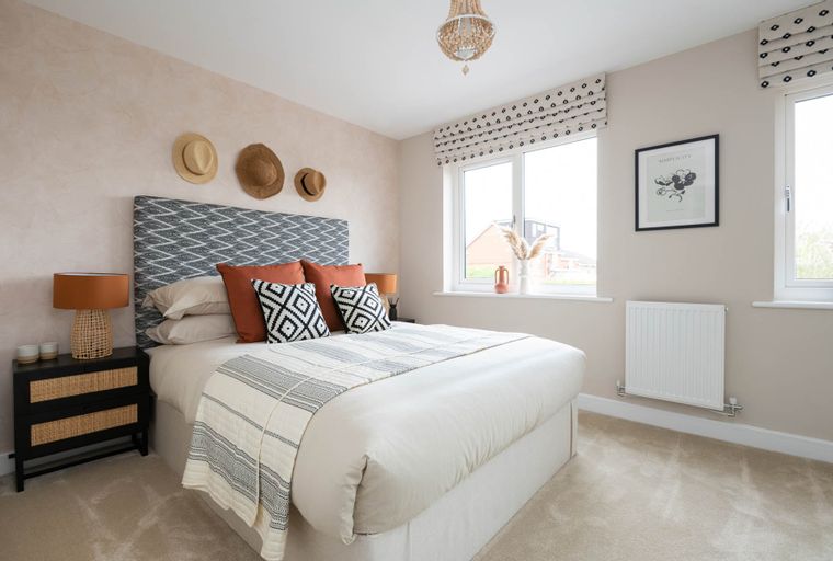 A bedroom with a bed, headboard, pillows, nightstand, lamp, and windows.