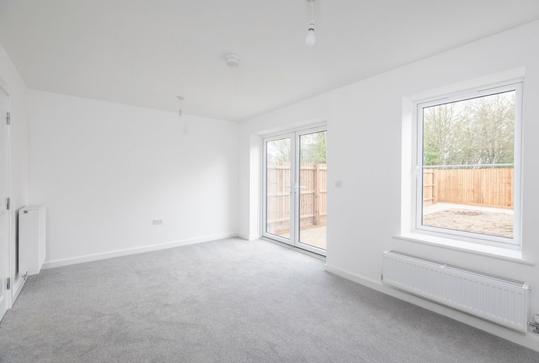 A room with grey carpet, white walls, double glass doors, and a window.