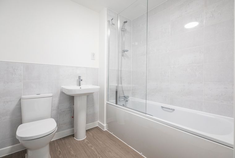 A bathroom with a toilet, sink, and bathtub with a shower screen.