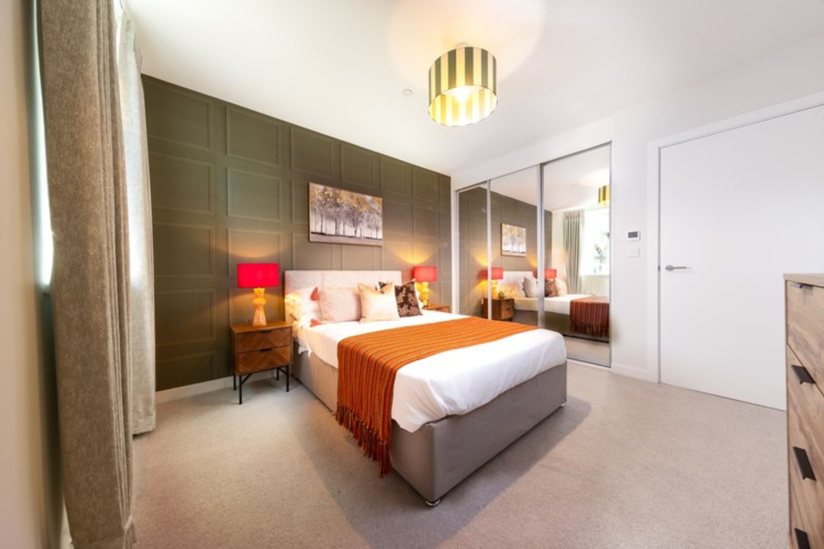 A bedroom with a bed, bedside tables, lamps, and mirrored wardrobes.