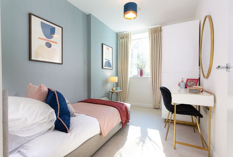 A bedroom with a single bed, a vanity desk, and a large window.