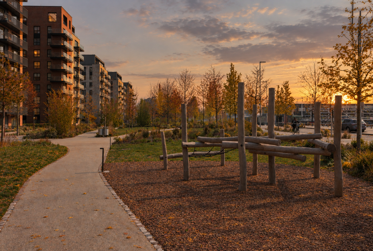 A modern apartment complex with a playground and a walking path during sunset.