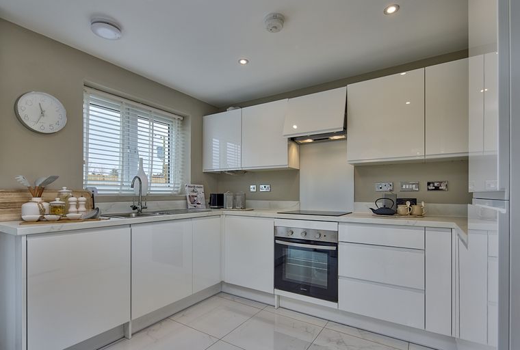 A modern white kitchen with sleek cabinets, a sink, and an oven.