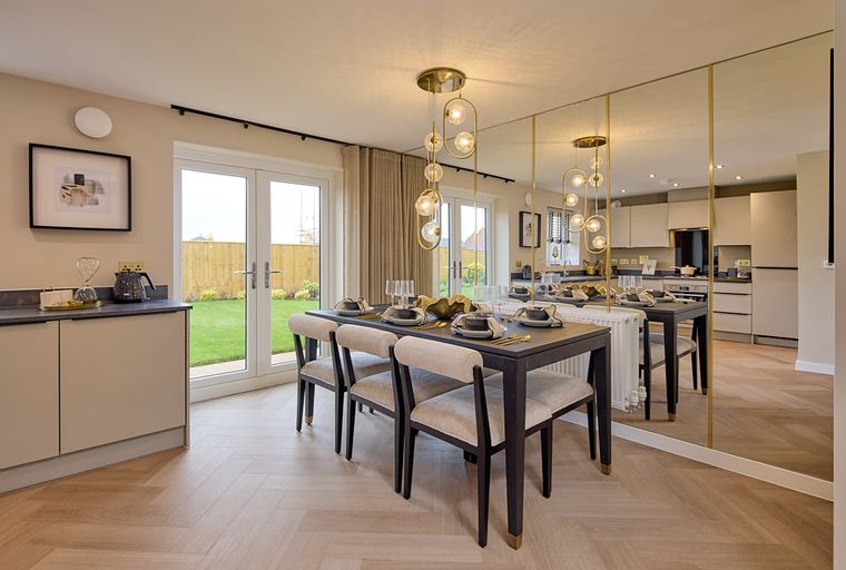 A dining room with a table set for a meal, chairs, a pendant light, and a mirrored wall.