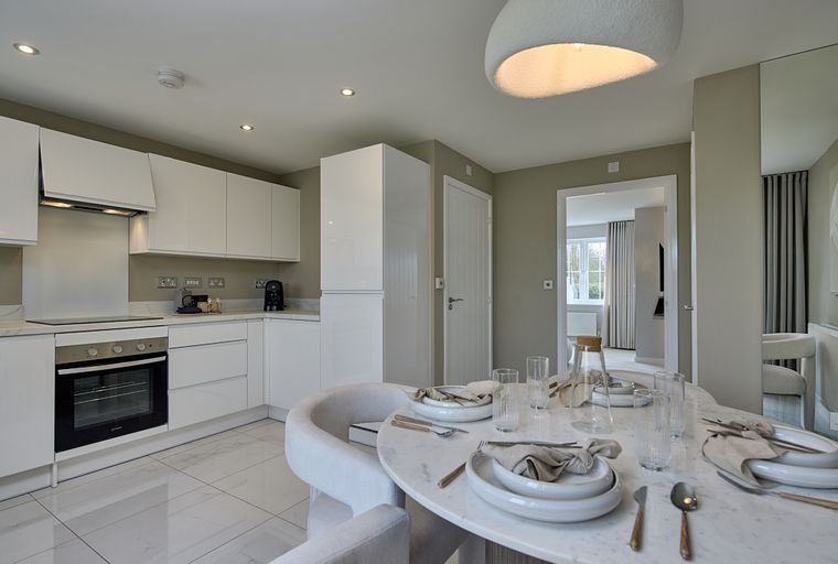 A modern kitchen and dining area with white cabinets, an oven, and a marble dining table set for a meal.