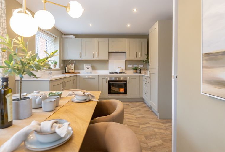 A modern kitchen and dining area with sage-green cabinets, an oven, a stovetop, and a dining table.
