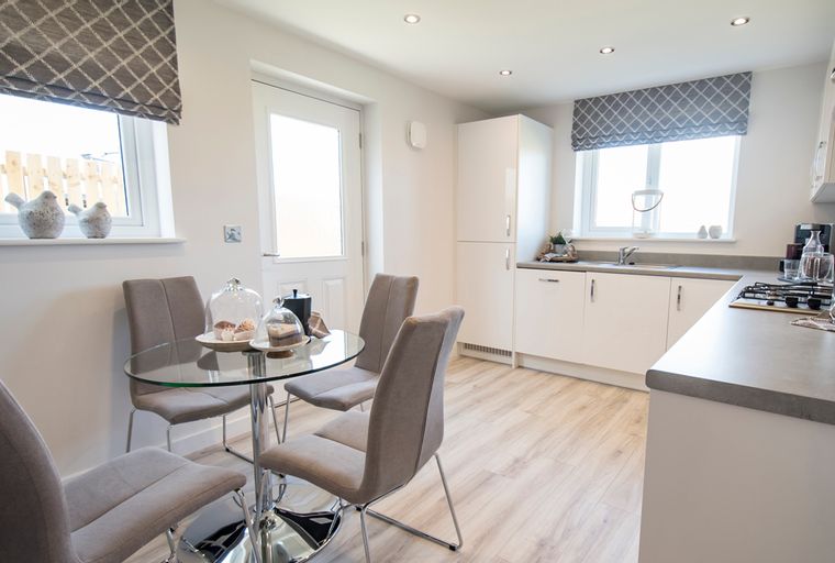 A dining area and kitchen with a glass-top table, chairs, white cabinets, and a sink.