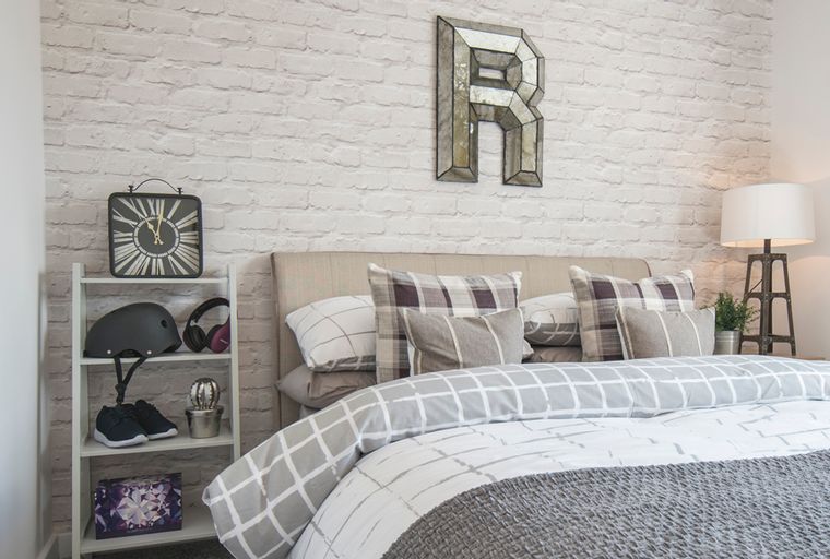 A bedroom with a bed, pillows, a shelf with items, and a lamp.