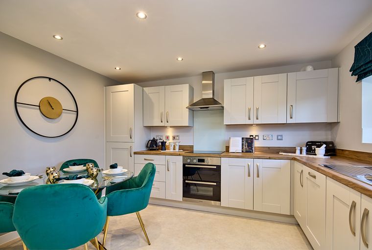 A modern kitchen and dining area with light gray cabinets, a glass dining table, and teal chairs.