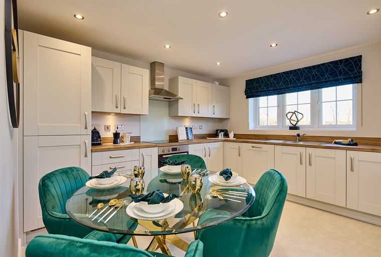 A dining area and kitchen with a glass table, green chairs, and white cabinets.
