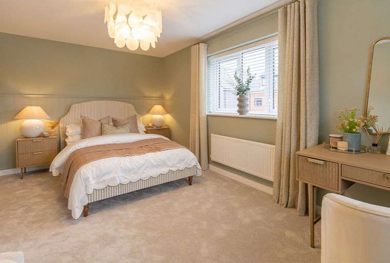 A bedroom with a bed, bedside tables, lamps, a window with curtains, and a vanity table.