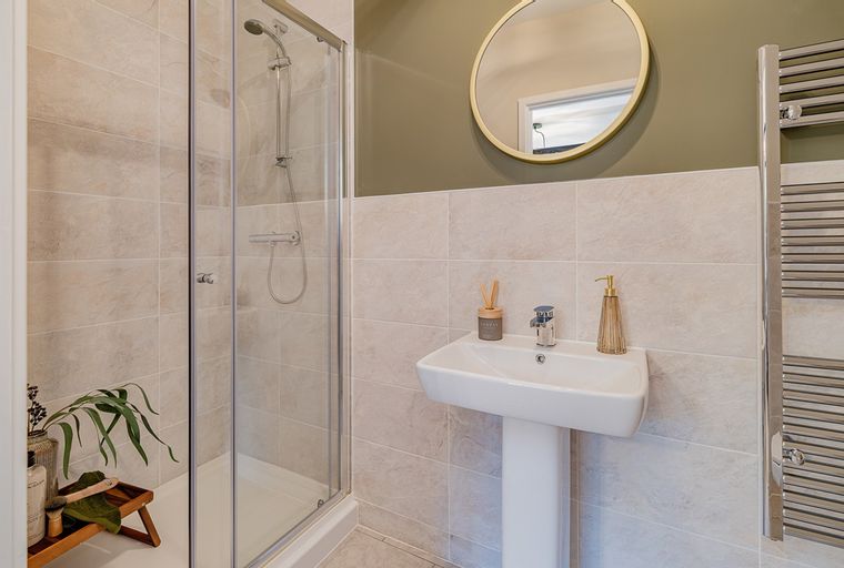 A bathroom with a shower, sink, mirror, and towel warmer.