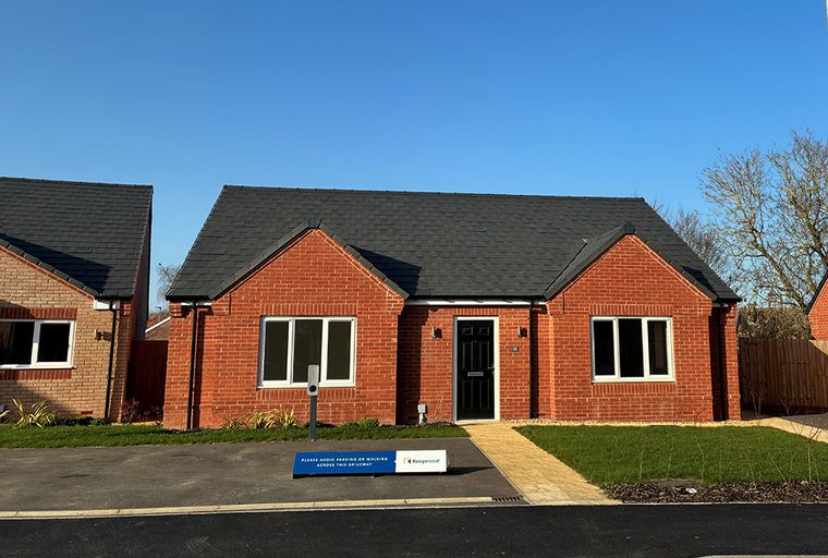 A red brick bungalow with a black front door and white-framed windows under a grey tiled roof.