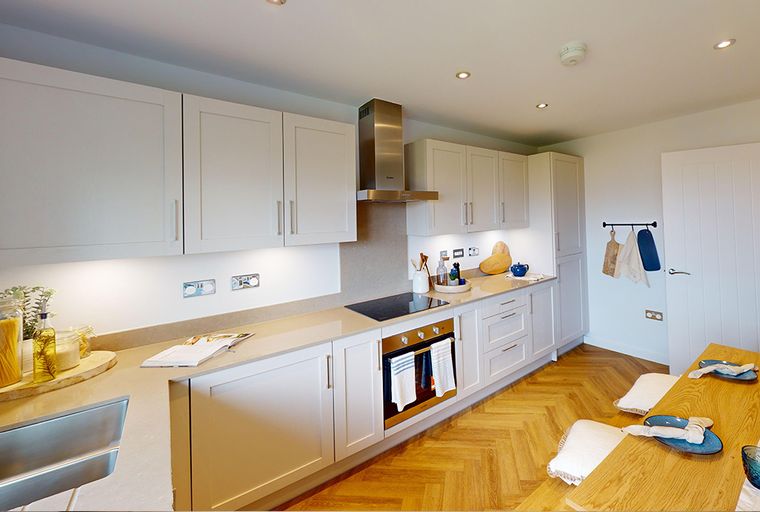 A modern kitchen with white cabinets, a stainless steel extractor hood, and a wooden floor.