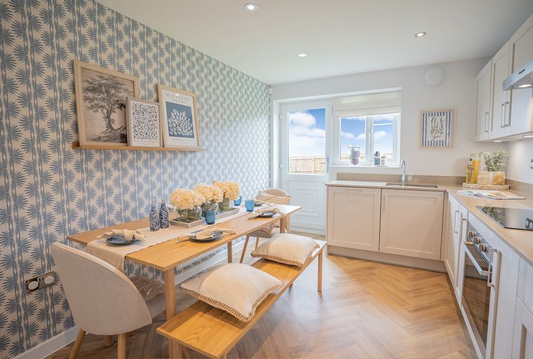A dining area and kitchen with blue and white wallpaper, a wooden table, and modern cabinetry.