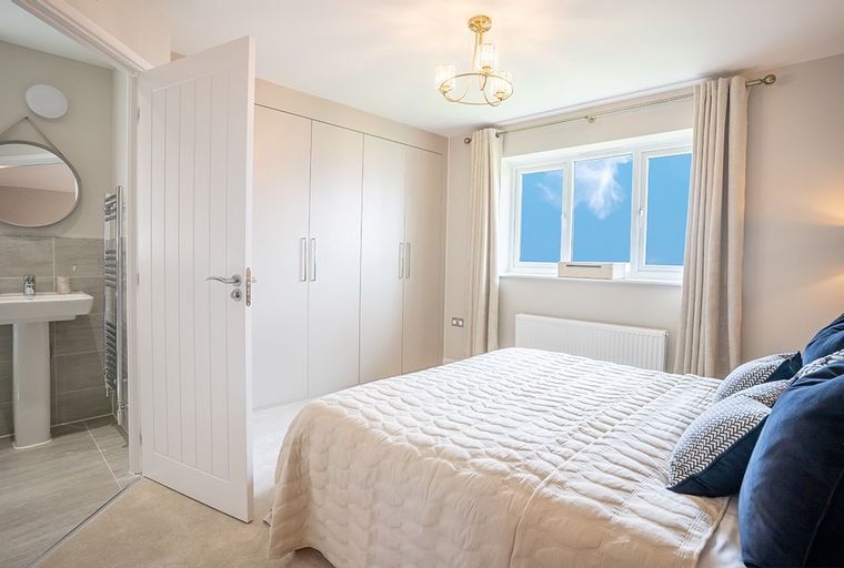 A bedroom with a bed, a wardrobe, a window, and an adjacent bathroom.