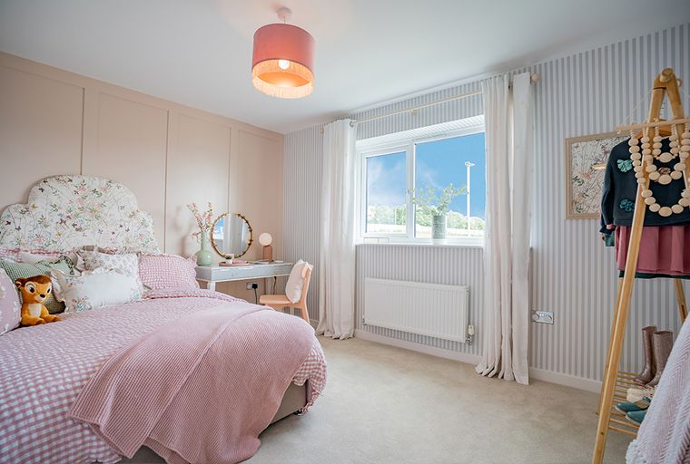 A bedroom with a bed, vanity, and window.