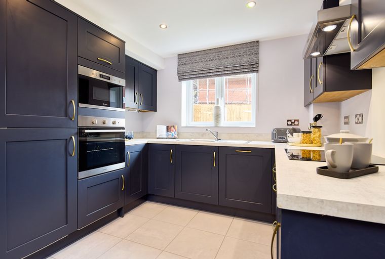 A modern kitchen with dark navy cabinets, integrated appliances, and a window.