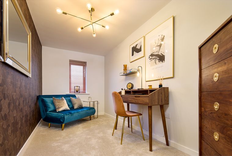 A room with a teal sofa, a desk, and artwork.