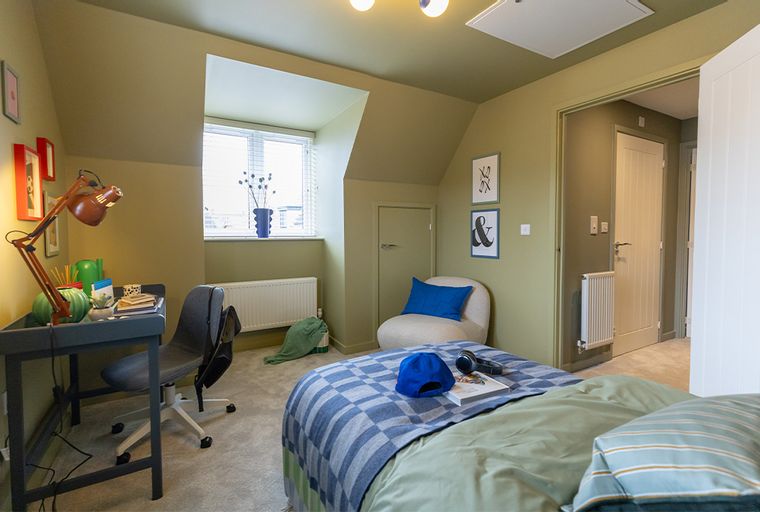 A bedroom with a desk, chair, bed, and armchair.