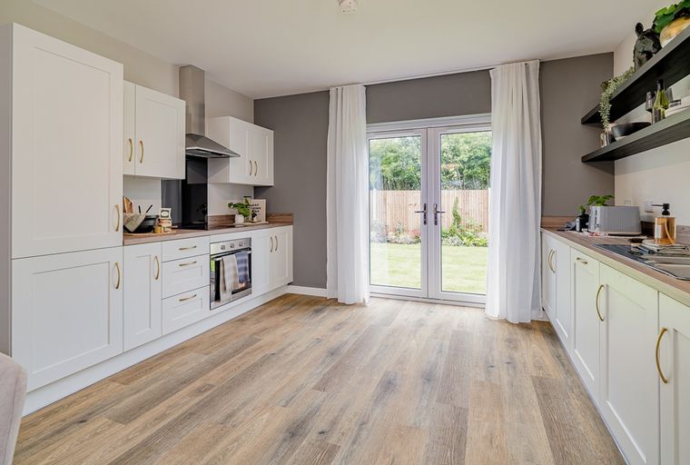 A modern kitchen with white cabinets, an oven, and French doors leading to a garden.