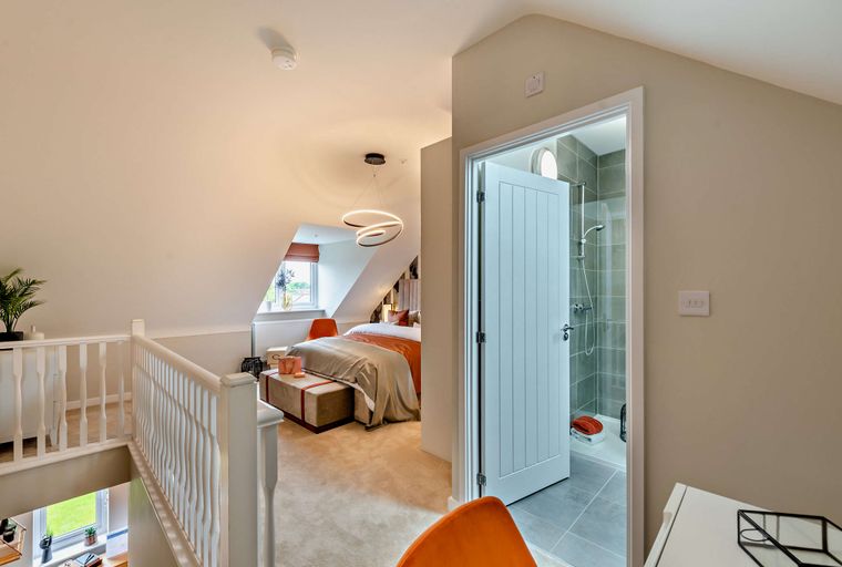 A bedroom with a bed, an ensuite bathroom, and a staircase railing.
