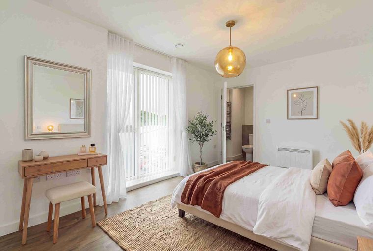 A bedroom with a bed, vanity, and a large window.
