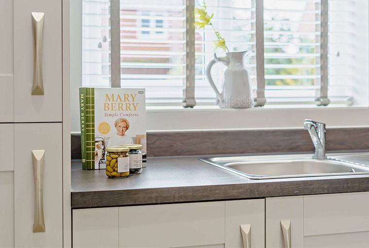 A kitchen counter with a sink, a cookbook, and jars of olives.