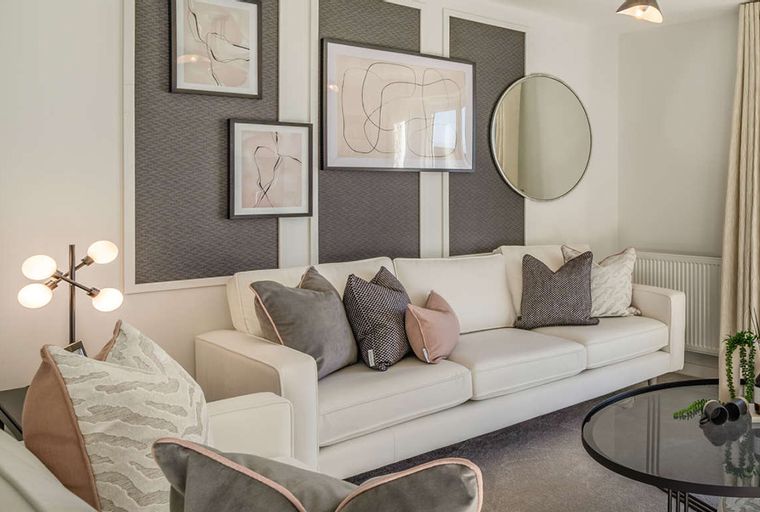A living room with a white sofa, decorative pillows, framed art, a mirror, and a floor lamp.