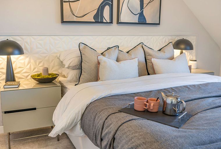 A bedroom with a bed, pillows, bedside tables, and lamps.