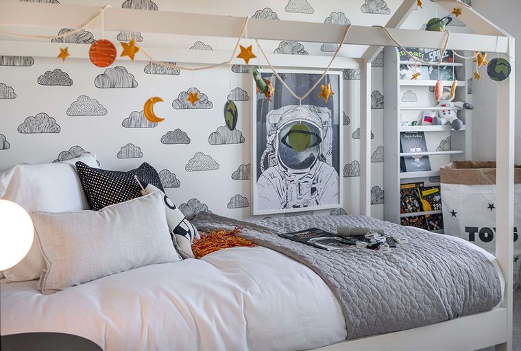 A bedroom with a bed, pillows, a bookshelf, and astronaut-themed decor.