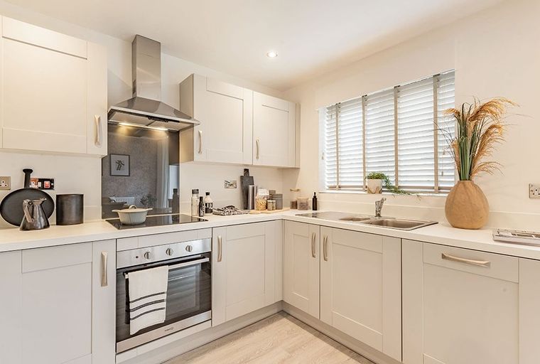 A modern kitchen with light-colored cabinets, an induction hob, an oven, and a sink under a window.