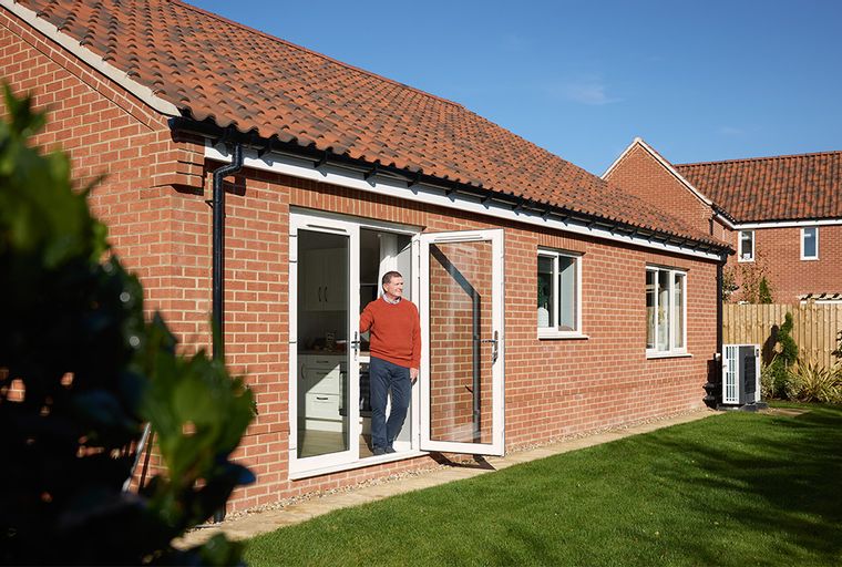 A man stands in the doorway of a brick house with a green lawn.
