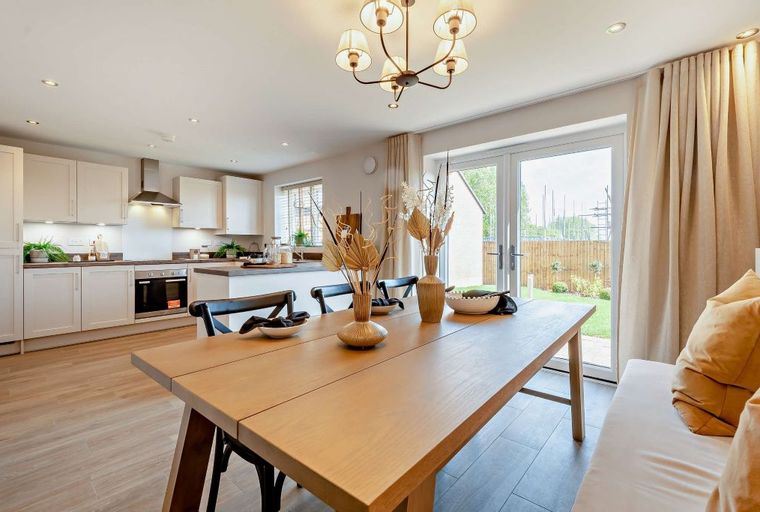 A dining table and chairs in front of a kitchen and sliding glass doors leading to a garden.