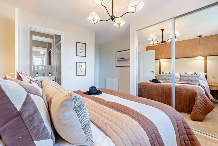 A bedroom with a bed, pillows, a hat, and mirrored closet doors.