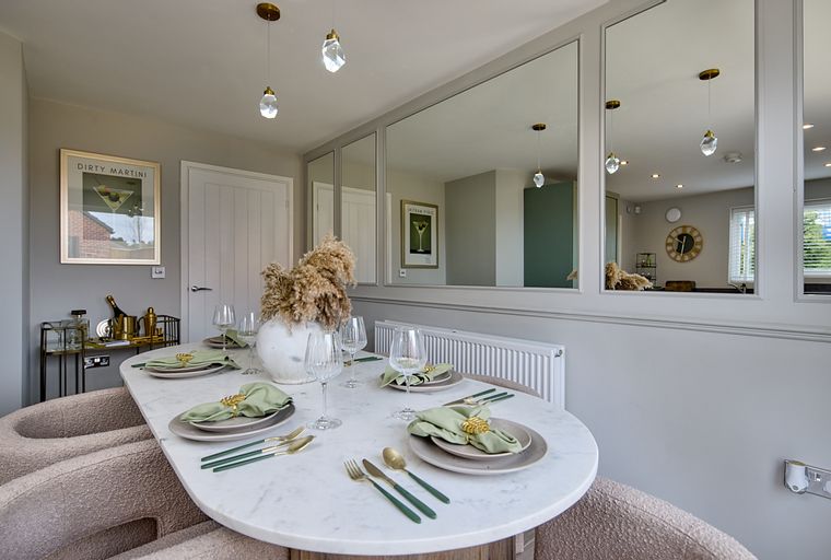 A dining table set for four with green napkins and gold cutlery.