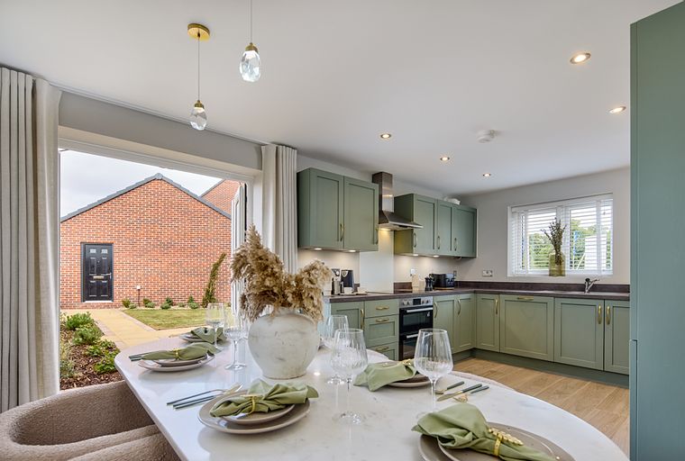 A dining table set for a meal in front of a kitchen with green cabinets.