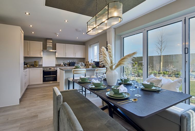 A dining area and kitchen with a table set for a meal and a view of a garden through large glass doors.