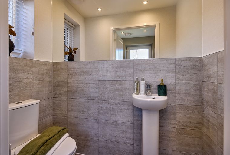 A toilet and a pedestal sink in a bathroom with grey tiled walls and a large mirror.