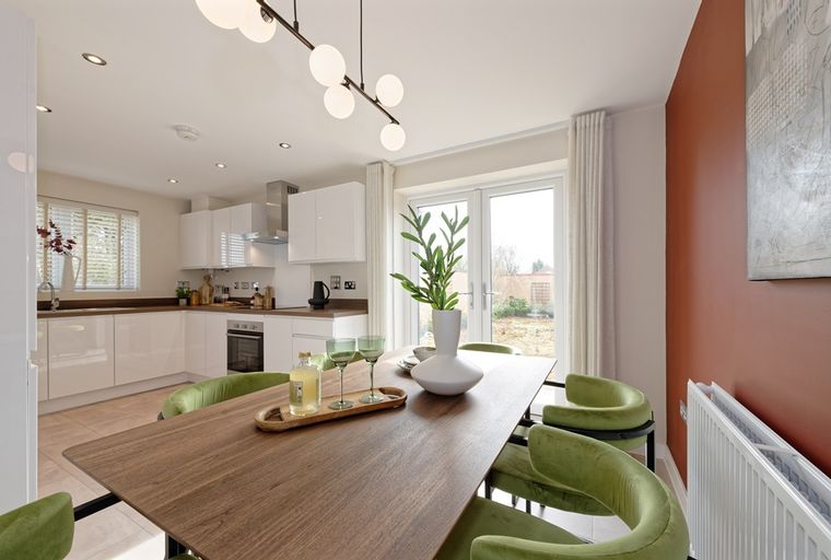 A dining area and kitchen with white cabinets, a wooden table, and green chairs.