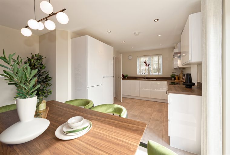 A modern kitchen and dining area with white cabinets, a wooden table, and green chairs.