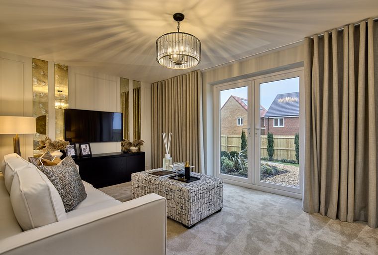 A living room with a sofa, ottoman, television, and French doors leading to a garden.