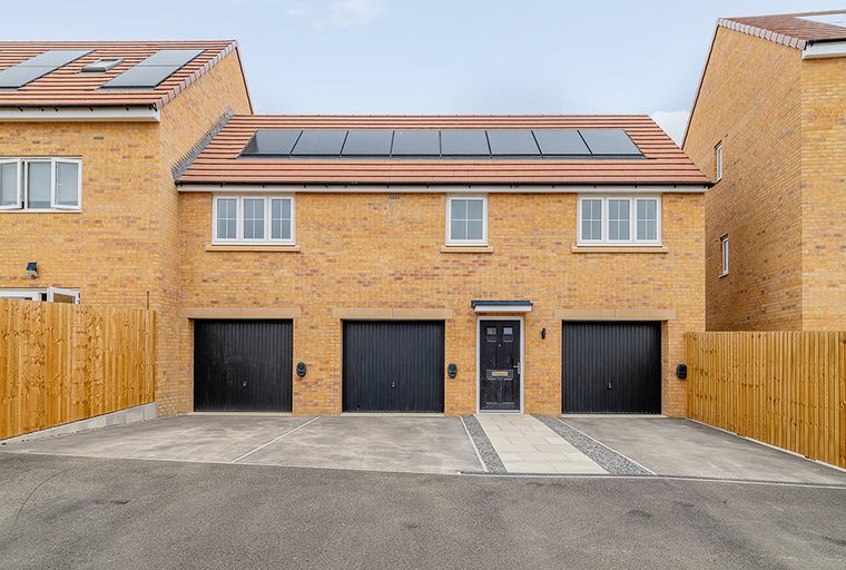 A yellow brick townhouse with three black garage doors and a black front door.