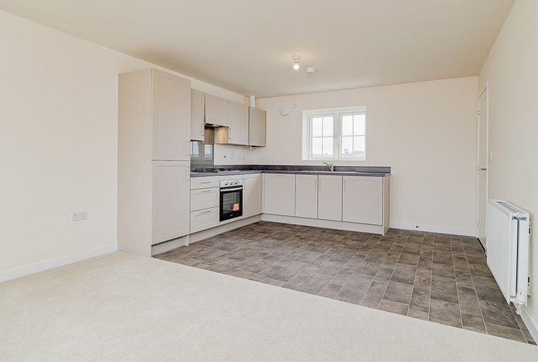 A kitchen and living area with light grey cabinets, a gas hob, an oven, a sink, a window, and tiled flooring.