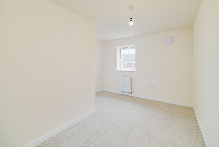 A bedroom with a window, radiator, and carpet.