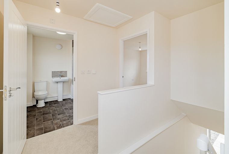 A hallway with an open doorway leading to a bathroom and a staircase with a banister.