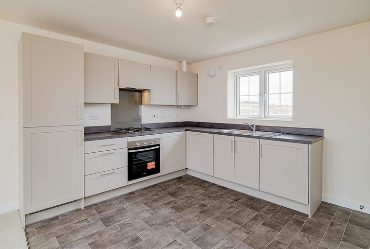 A kitchen with light-colored cabinets, a dark countertop, a gas hob, an oven, and a sink under a window.