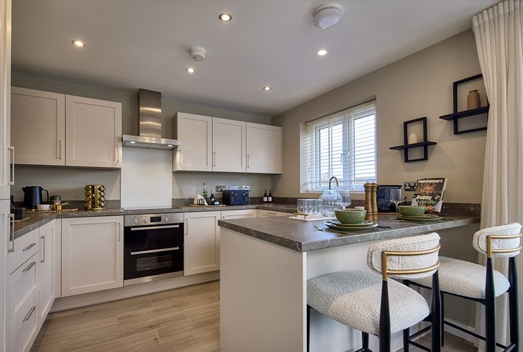 A modern kitchen with light-colored cabinets, a stainless steel range hood, and an island with bar stools.