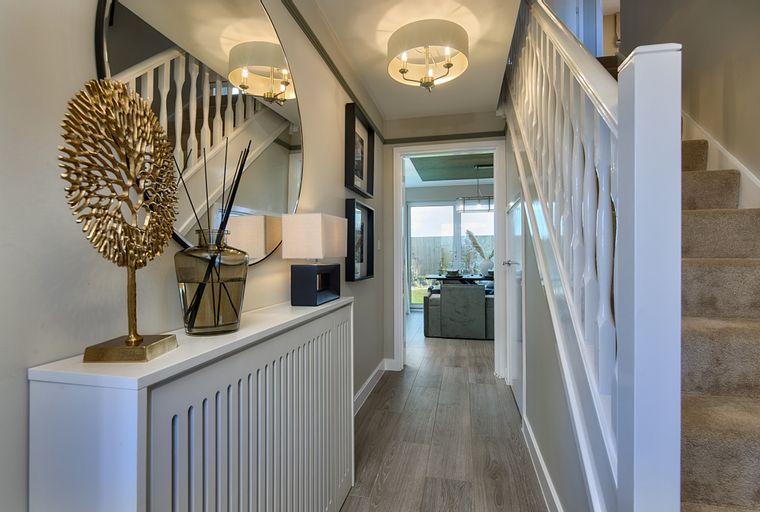 A hallway with a staircase, a mirror, and decorative items on a radiator cover.